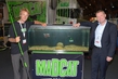 Jakub Vagner (links) mit neuer Madcat-Wallerrute und DAM-Boss Jesper Bach Sørensen vor einem Wels-Aquarium, in dem der neue DAM-Clonk Teaser auf Tauchstation geht.